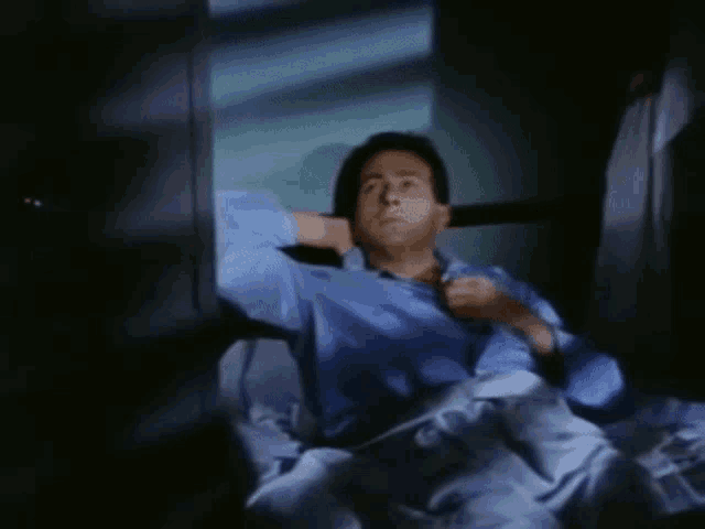 a man in a blue shirt sits in a dark room