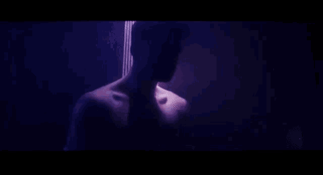 a shirtless man is standing in front of a purple light .