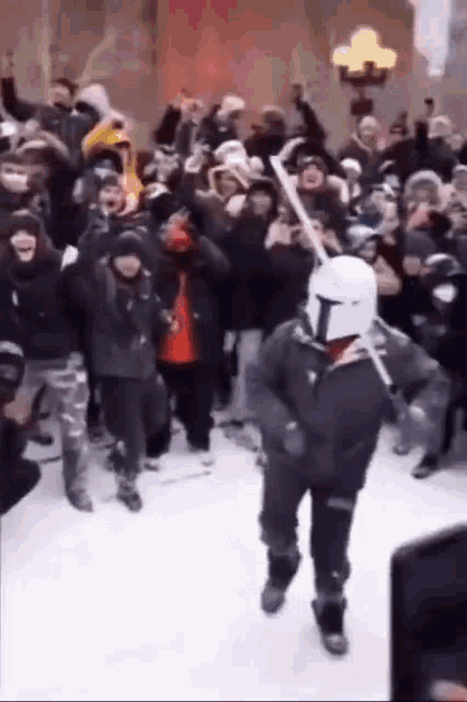 a man in a mandalorian helmet is walking through a crowd of people .