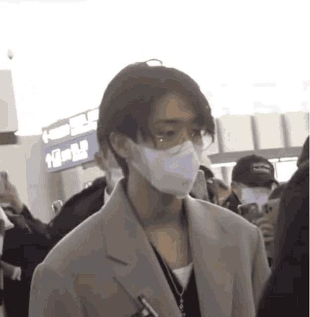 a man wearing a mask and glasses is walking through a crowd of people .