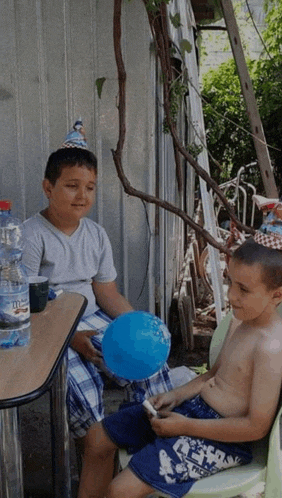 two young boys wearing party hats sit at a table with a bottle of water