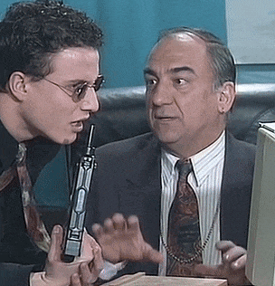 a man in a suit and tie is talking to another man holding a gun