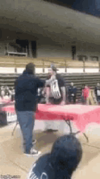a man is standing next to a table in a gym talking to a woman .