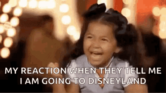 a little girl is crying and laughing while sitting in front of a disneyland sign .