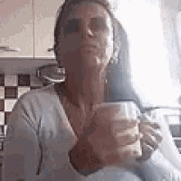 a woman is holding a cup of coffee in her hands in a kitchen .