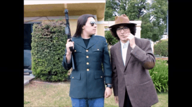 a man in a military uniform holds a gun next to another man in a suit and hat