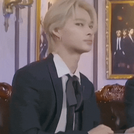 a man in a suit and tie is sitting in front of a picture on the wall .