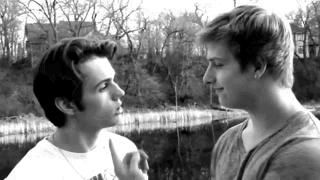 two young men are looking at each other in a black and white photo with trees in the background