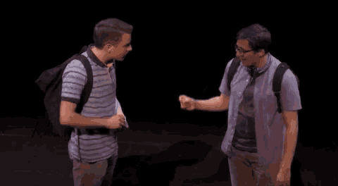 two men are standing next to each other on a stage in a dark room talking to each other .