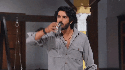 a man in a gray shirt is drinking from a glass