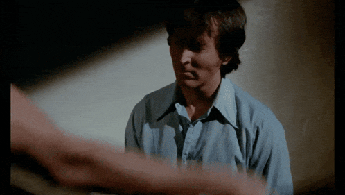 a man in a blue shirt is looking at another man 's hand