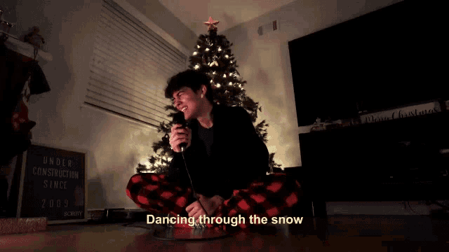a man singing into a microphone in front of a christmas tree with the words " dancing through the snow " below him