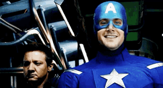 a man in a captain america costume smiles while another man looks on