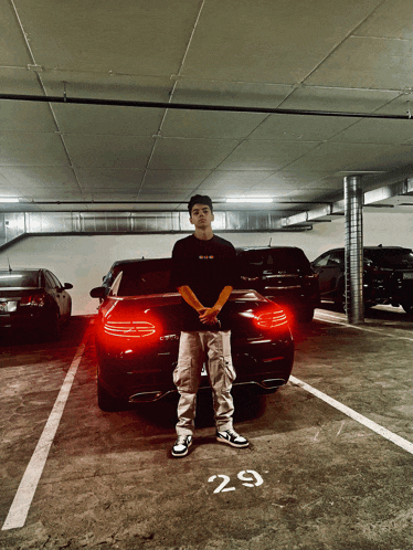 a young man stands in front of a car in a parking garage with the number 29 on the ground