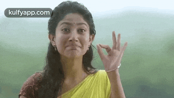 a woman in a yellow sari is giving an ok sign with her hand .
