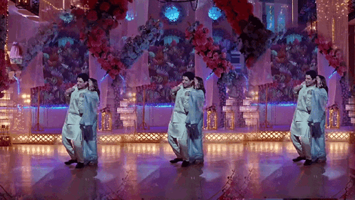 a group of people are dancing on a stage in front of flowers