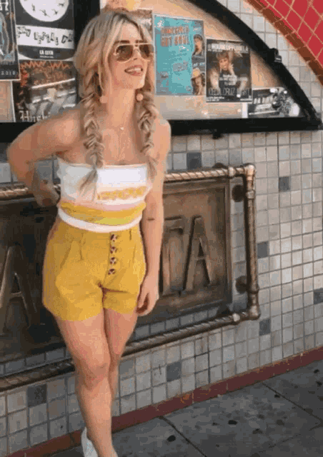 a woman wearing yellow shorts stands in front of a sign that says " a "