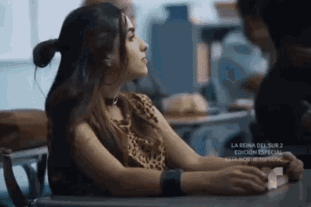 a woman in a leopard print top is sitting at a desk in a classroom with other people .