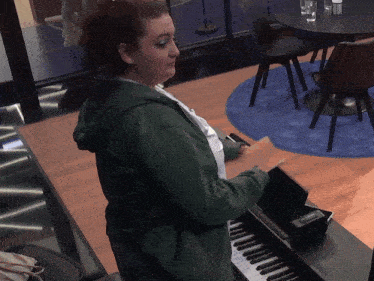 a woman in a green hoodie plays a piano