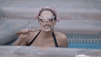 a woman is brushing her teeth in a pool while wearing sunglasses and a pink headband .