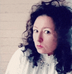 a woman with curly hair wearing a white shirt looks at the camera