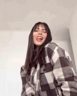 a woman wearing a plaid jacket is laughing and sticking her tongue out .