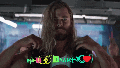 a man with long blonde hair and a beard is standing in front of a sign that says ' i m ' on it