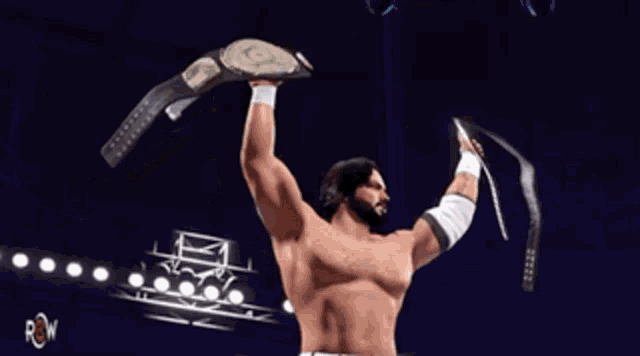 a shirtless wrestler holds up two championship belts in a dark arena