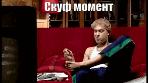 a man is sitting on a red couch with a foreign language written on the screen
