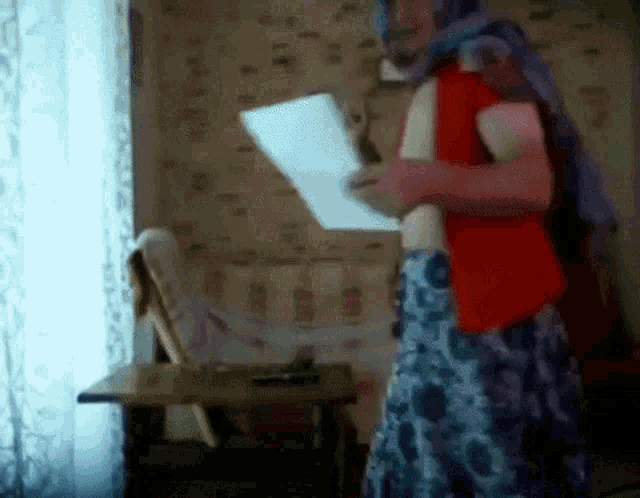 a woman in a red vest and blue skirt is holding a piece of paper in a room .