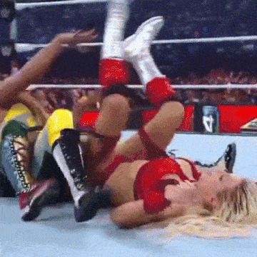 a woman is laying on her back in a wrestling ring while another woman holds her legs up .