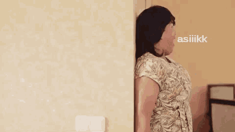 a woman is peeking out from behind a wall and making a face .