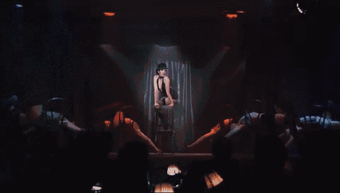 a woman in a black top hat is sitting on a stool