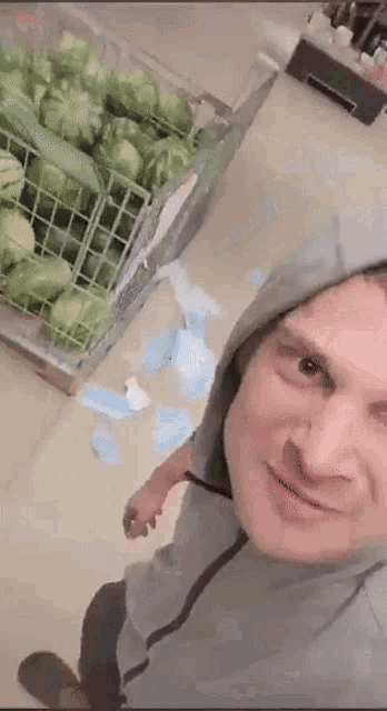 a man wearing a hoodie is standing in front of a crate of cabbage