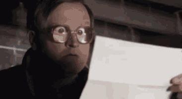 a man wearing glasses is holding a piece of paper and making a funny face .