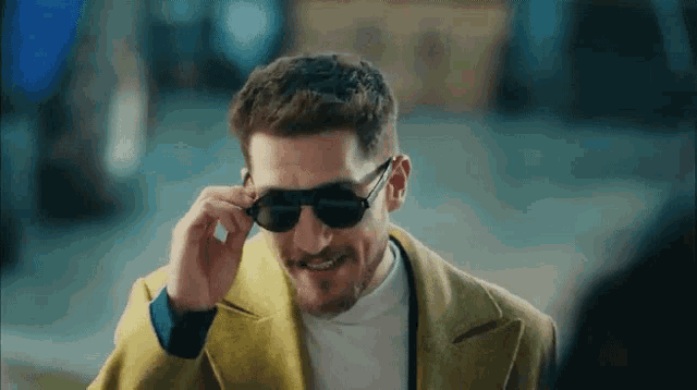a man wearing sunglasses and a yellow coat is smiling while talking on a cell phone .
