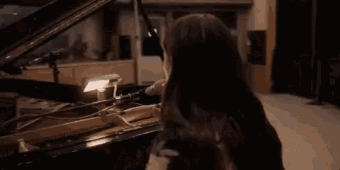 a woman playing a piano with another woman playing a guitar behind her