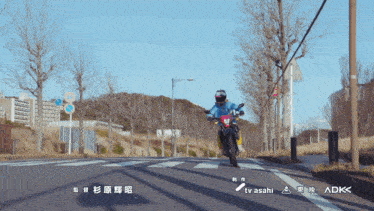 a person riding a motorcycle down a street with adk on the bottom