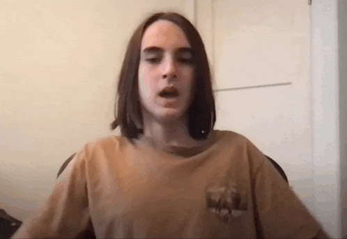 a young man with long hair wearing a brown t-shirt