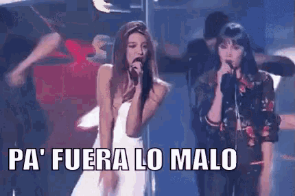 two women are singing into microphones on a stage and the words pa fuera lo malo are written below them .