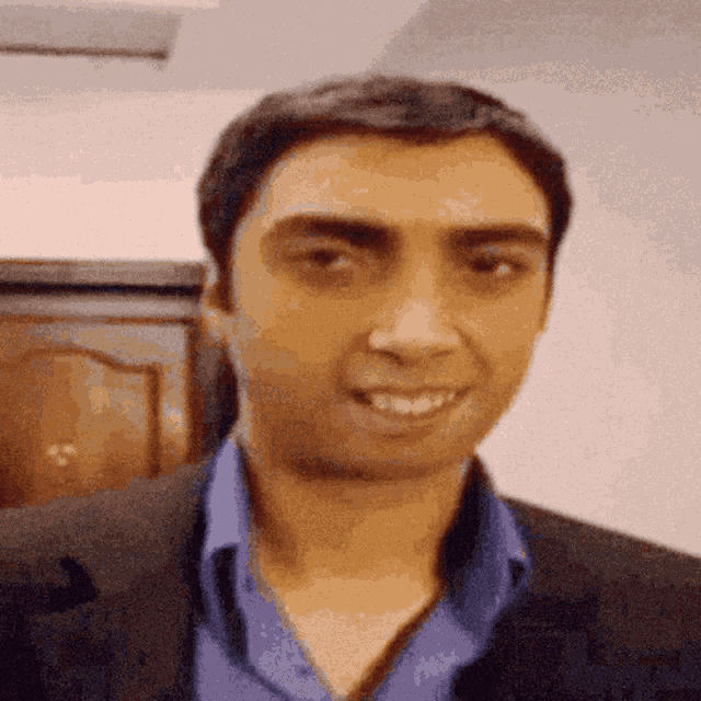 a man wearing a blue shirt and a black jacket smiles for the camera
