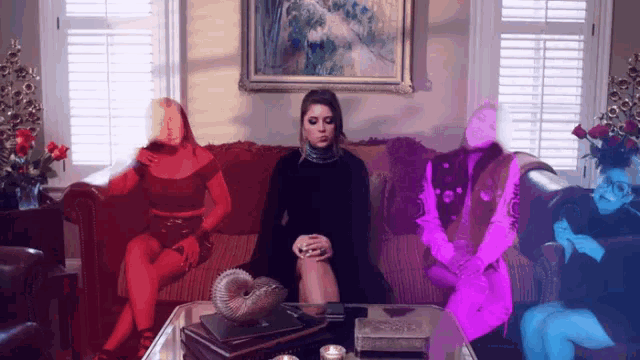a woman in a black dress sits on a couch surrounded by other people