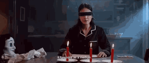 a woman is sitting at a table with candles and a puppet and says it functions as a medium