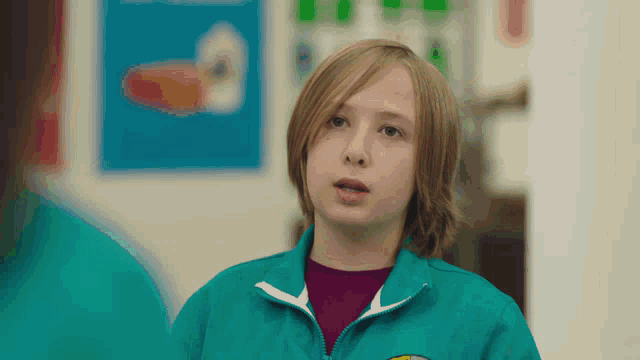 a young boy wearing a green jacket with a yellow sticker on the front