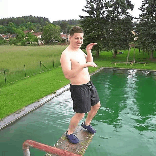 a shirtless man in black shorts is standing on a diving board