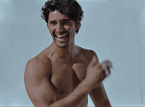 a shirtless man is smiling and clapping in front of a white wall