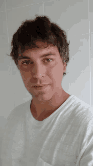 a man in a white t-shirt looks at the camera