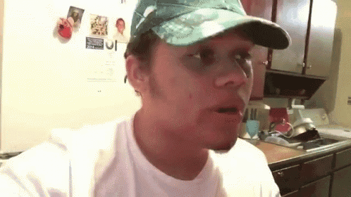 a man wearing a hat and a white shirt is standing in front of a refrigerator