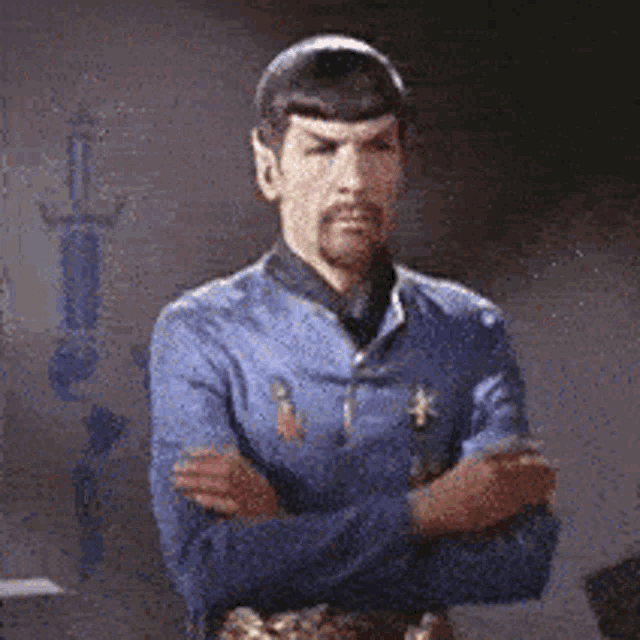 a man with a beard is standing with his arms crossed in a room .