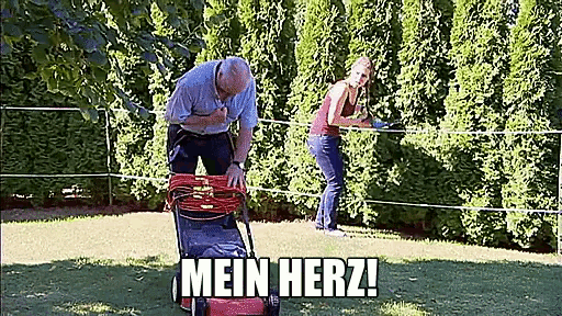 a man is pushing a lawn mower in a garden while a woman is cutting trees .